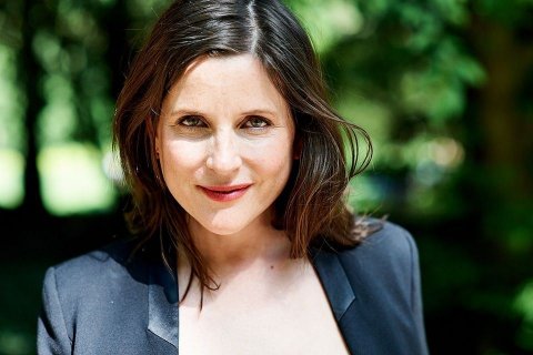 Die Autorin Ariadne von Schirach, Foto: Rahel Taeubert Das Bild zeigt eine Person mit schulterlangen braunen Haaren, die einen dunklen Blazer über einem hellen Oberteil trägt. Der Hintergrund besteht aus einer natürlichen Umgebung mit verschwommenem Grün, das auf das Vorhandensein von Bäumen oder Laub hinweist.