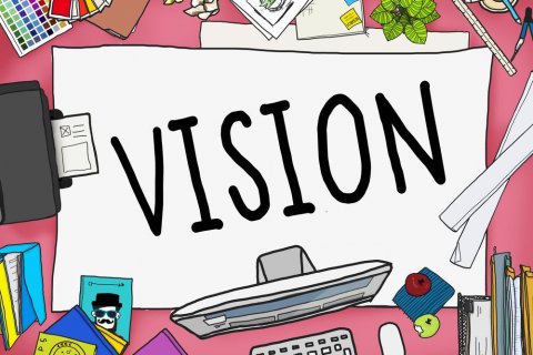 Motiv: Rawpixel.com / shutterstock Cartoon-Darstellung einer Schreibtischoberfläche, auf der viele Dinge ausgebreitet liegen - u.a. Briefumschläge, Stifte, ein Lineal, ein Farbfächer, Bücher, ein Monitor, eine Tastatur und ein Drucker. In der Mitte liegt jedoch ein großes weißes Blatt, auf dem in schwarzen Großbuchstaben das Wort "VISION" steht.