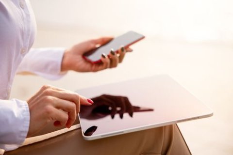 Die Arme einer Person sind zu sehen. In der linken Hand ein Smartphone und mit der rechten bedient sie ein Tablet.