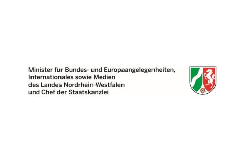 Auf hellem Hintergrund steht links ein mehrzeiliger schwarzer Text: &bdquo;Minister f&uuml;r Bundes- und Europaangelegenheiten, Internationales sowie Medien des Landes Nordrhein-Westfalen und Chef der Staatskanzlei&ldquo;. Rechts daneben befindet sich das farbige Landeswappen Nordrhein-Westfalens: links ein gr&uuml;nes Feld mit wei&szlig;er Wellenlinie, rechts ein rotes Feld mit wei&szlig;em Pferd, darunter eine kleine Rose. Das Layout ist klar und offiziell.