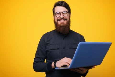 Ein Mann vor einem gelben Hintergrund. Er h&auml;lt einen aufgeklappten Laptop in beiden H&auml;nden.