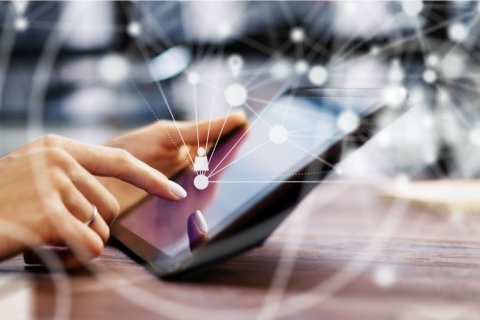 Auf dem Bild sieht man eine Hand, die ein Tablet bedient. Symbolhaft ist eine Art Netz &uuml;ber dem Tablet gespannt, was f&uuml;r Vernetzung und das Internet steht. 